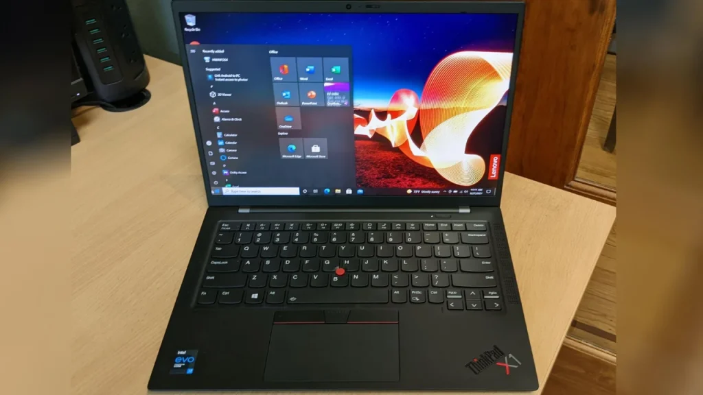 Top 10 Laptop Brands in 2026. A black Lenovo ThinkPad laptop open on a wooden desk, showing the Windows start menu on the screen and the signature red trackpoint on the keyboard.