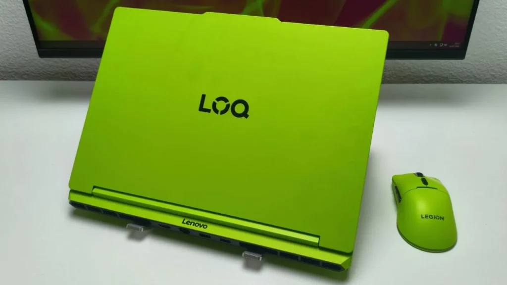 A Lenovo LOQ 15 laptop displayed closed on a white stand, featuring a bright lime green top cover and logo, with a matching lime green gaming mouse placed beside it on a white desk.