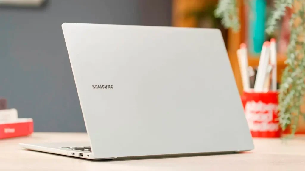 Top 10 Laptop Brands in 2026. A sleek, silver Samsung laptop, viewed from the rear corner, resting on a desk with a blurred office background.